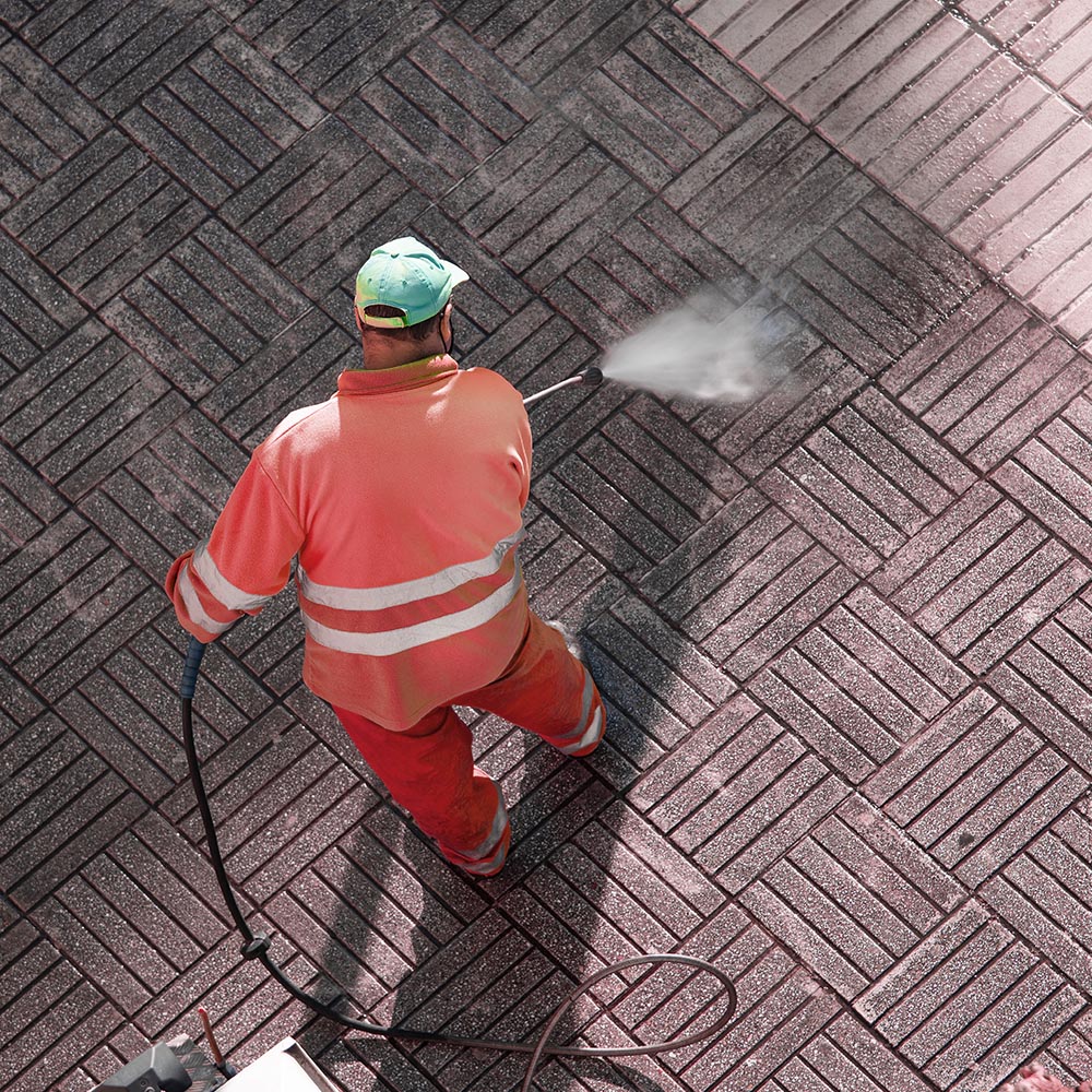 a man in uniform is pressure washing a brick walkway
